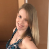 Smiling person indoors with straight blonde hair in a sleeveless floral top, turned toward the camera against tan walls—portrait for a blog on burnout relief and stress management.