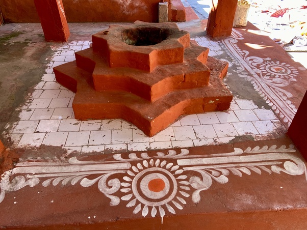 Stepped, star-shaped terracotta havan kund on a tiled courtyard with white rangoli borders, seen during travel through Gangotri in the Himalaya en route to Gaumukh, reflecting Living Dharma in practice.