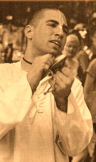Sepia-toned photo of a person in a loose, traditional shirt, eyes closed, tapping small hand cymbals during a lively street gathering; a rhythmic, candid moment featured in our Articles post.