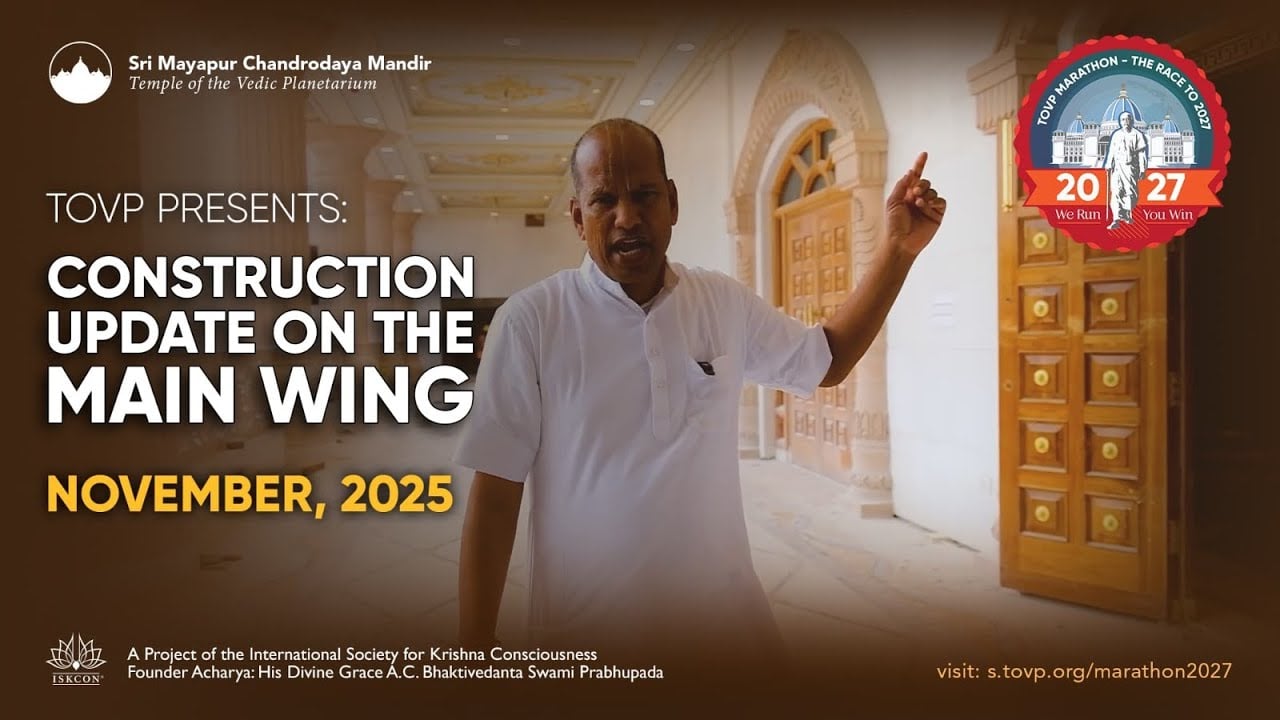 Temple of the Vedic Planetarium main wing corridor with ornate doors and carved arches; a guide gestures during the TOVP construction update, November 2025, with a Marathon 2027 badge; testing feed image.