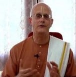 A bald speaker in a simple robe sits indoors before soft curtains, wearing glasses and a lapel microphone, gesturing mid-lecture during an ATL Sunday Feast event; image prepared for testing.