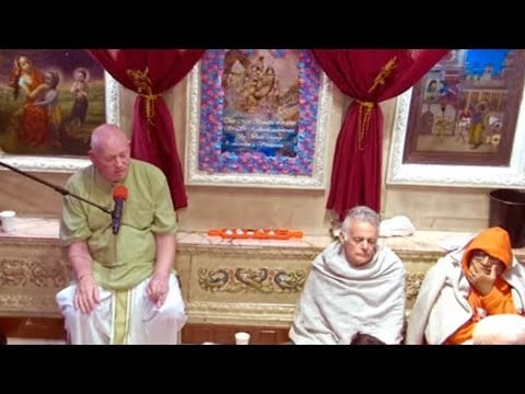 Inside an ornate ISKCON London temple, three devotees sit before deity paintings and red curtains; one speaks into a microphone during prayers and a special evening class; testing event context.