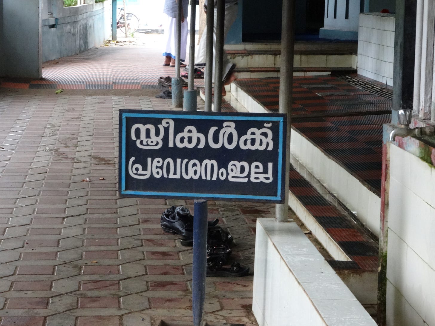 Malayalam sign at a Kerala temple entrance reading 'No entry for women', beside a tiled walkway and removed shoes, setting the scene for Kerala history and the Cheraman Perumal legend.