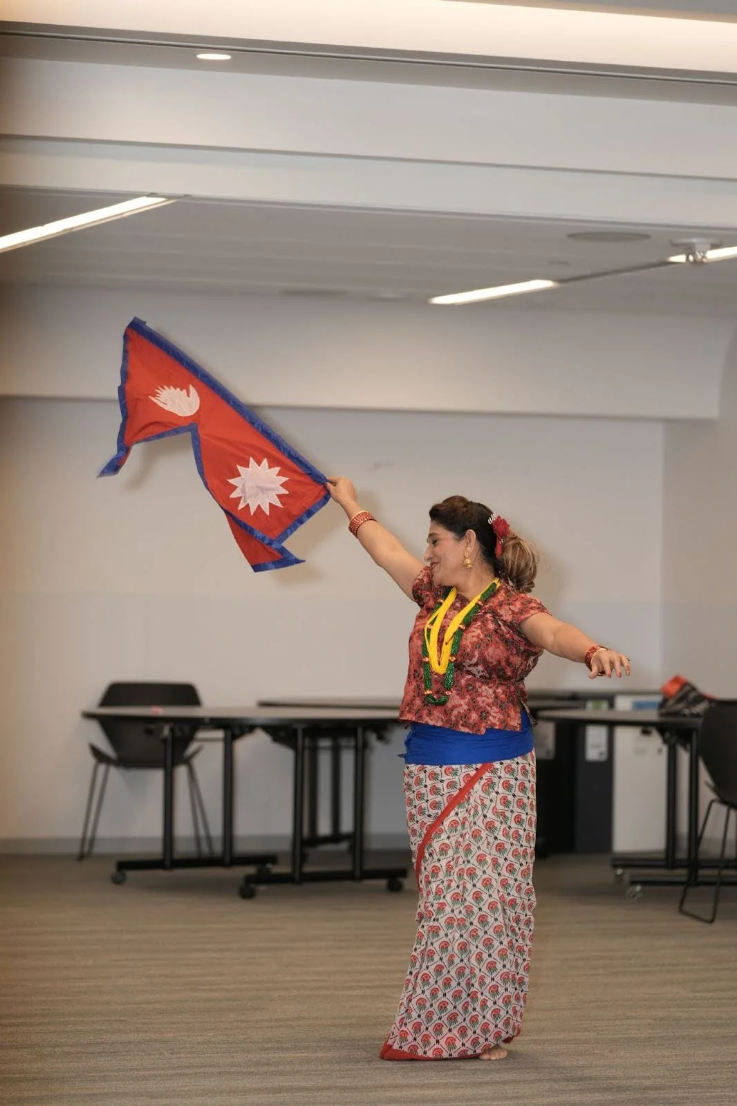 Dancer in traditional South Asian attire waves the Nepal flag indoors during a cultural performance, barefoot and smiling, at a Hindu Heritage Month 2025 community event in Edmonton. Cohna Blog.