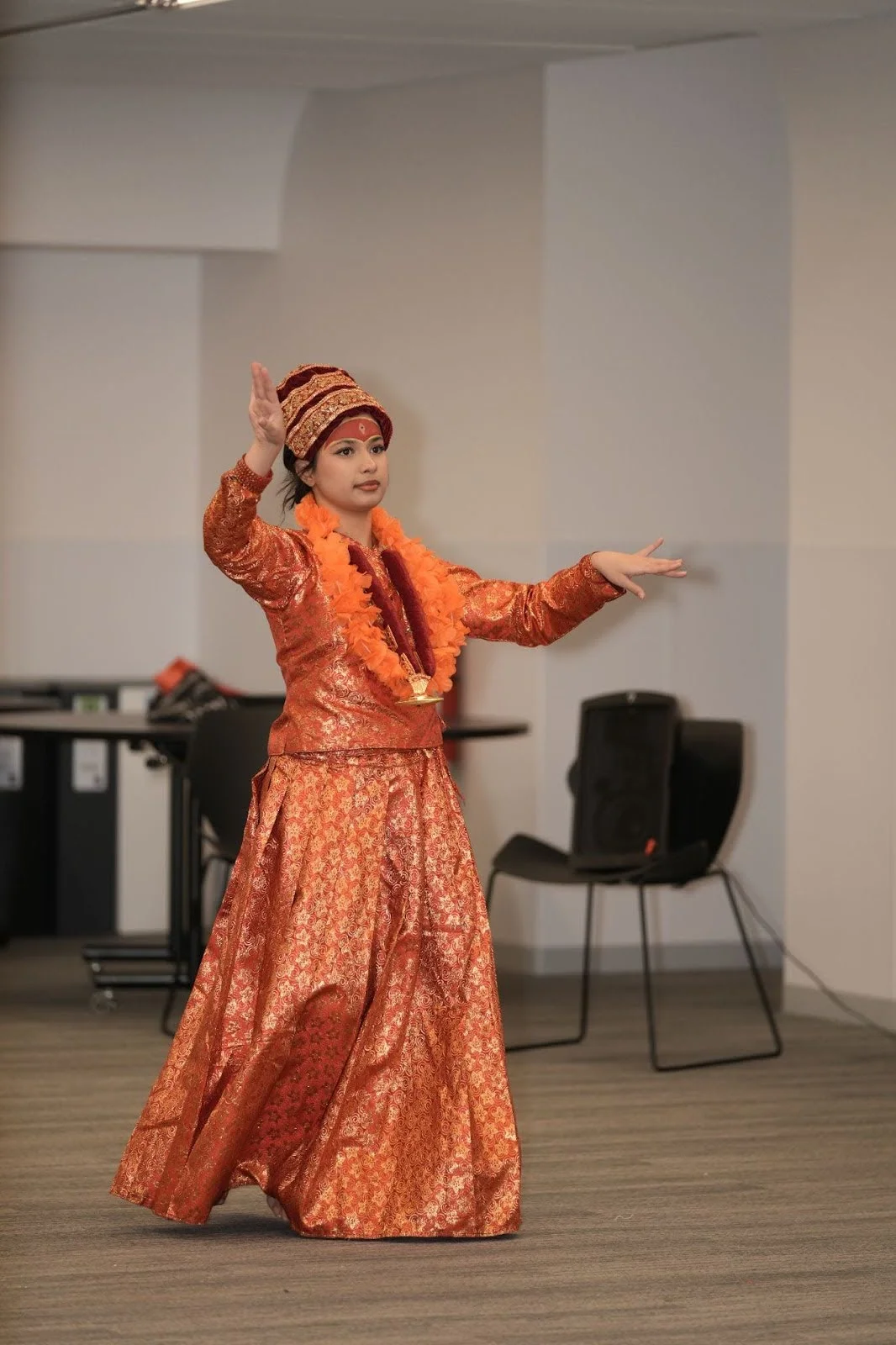 Dancer in shimmering orange traditional costume performs a classical Hindu dance indoors in Edmonton, arms extended mid-gesture, honoring Hindu Heritage Month 2025 community celebrations.