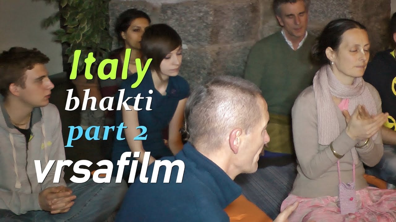 Small group seated indoors during a Hare Krishna bhakti gathering in Italy; people clap and chant with eyes closed; on-screen text reads “Italy bhakti part 2 vrsafilm.” Shared in testing category.