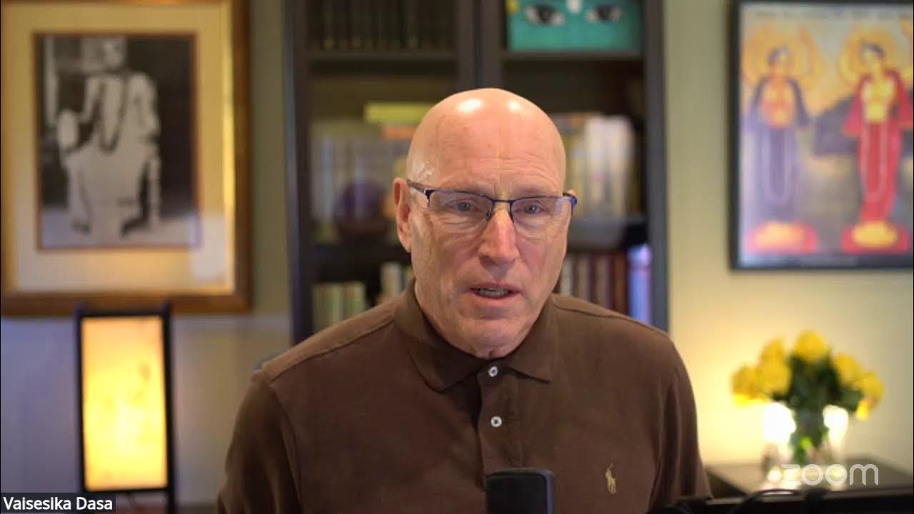 Zoom livestream shows a bald man with glasses in a brown polo, speaking into a microphone before bookshelves, framed art, a soft lamp, and yellow flowers during Success Sadhana: Get Grounded, testing.