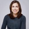 Headshot of a smiling person in a charcoal sweater against a light gray background for a blog on expectations, change & challenges, loss, disappointment, letting go, and happiness.