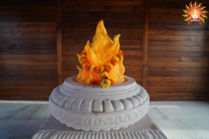 Garlanded orange-yellow flame sculpture on an intricately carved stone pedestal before wooden panels; image for Analysis/Insights and News updates on the Akhand Jyoti debate at Ayodhya's ram temple.