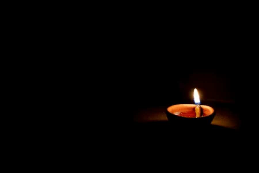 Single earthen oil lamp (diya) with a steady cotton-wick flame against a dark background, pooling warm light on the floor; a quiet, meditative scene linked to Hindu worship and Living Dharma.