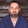 Close-up portrait of a bearded adult with a calm expression against dark wooden planks, illustrating a blog on anxiety, mental health, Mindfulness, self-care, and wisdom from change & challenges.