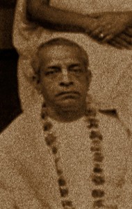 Sepia portrait of a seated elder in simple robes and a flower garland, facing forward with a calm, solemn expression; devotional setting, chest-up crop - for A.C.B. Swami Prabhupada Articles.