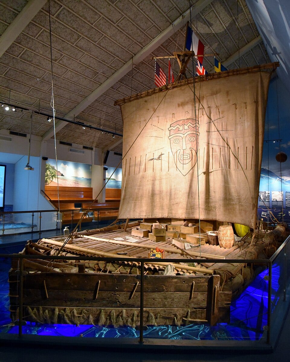 Exhibit of the Kon-Tiki balsa-wood raft, with lashed logs, cargo boxes, and a tall canvas sail painted with a tiki face - icon of Thor Heyerdahl's 1947 Pacific expedition and 5,000-mile crossing.