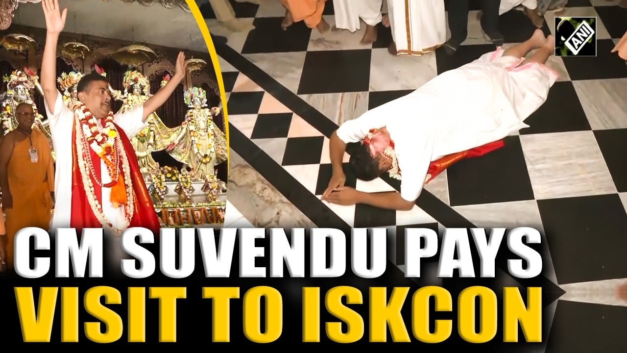 Inside ISKCON Mayapur, West Bengal, a garlanded devotee in white and red raises his arms during Aarti before ornate deities, as another lies prostrate on a black-and-white marble floor; testing