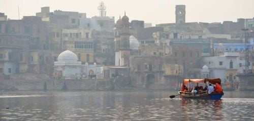 Hazy riverside cityscape with domed and arched buildings; a small oar-powered boat with an orange canopy ferries passengers across calm water—useful for visual testing of haze and contrast.
