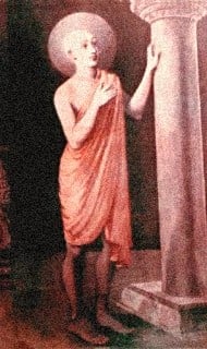 Painting of a saffron-robed saint with halo, standing barefoot beside a stone pillar, one hand on his heart and one on the column, evoking humble bhakti and meditation on Sri Krishna for Articles.