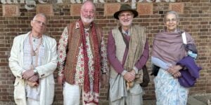 Four adults stand in a row before a brick wall, wearing patterned shirts, shawls, and a hat; one holds a cane and another a folded wrap. A candid group portrait included for the testing category.