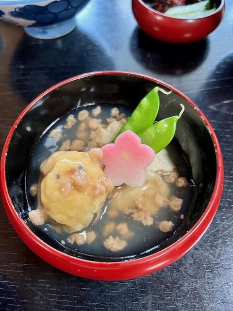 Japanese soup in a red lacquer bowl with greens and a pink flower garnish, evoking Kyoto dharma tradition and guru yoga during Gion Matsuri.