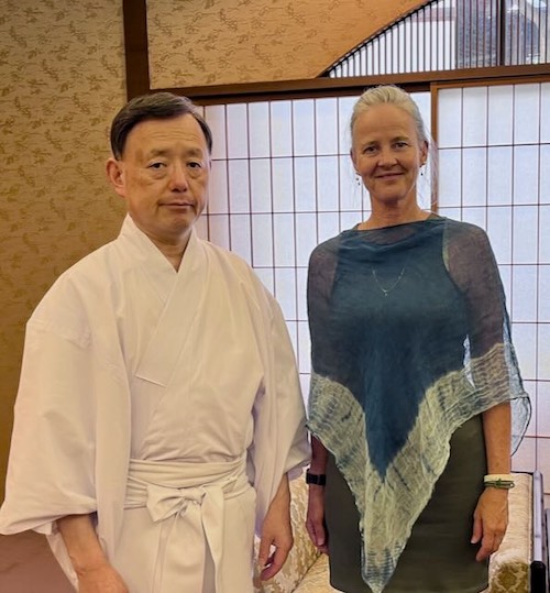 A robed Japanese spiritual mentor stands with a woman in a teal shawl before shoji screens in Kyoto, reflecting guru yoga and Dharma tradition.