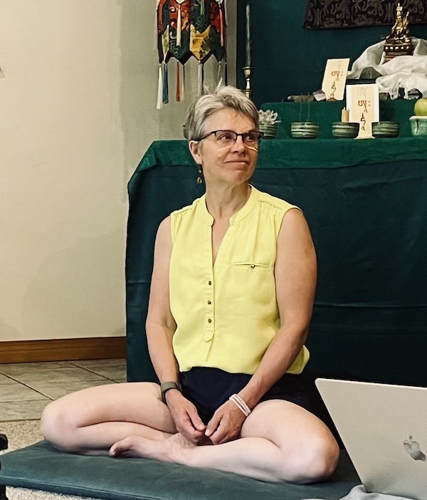 Maureen Smith sits cross-legged on a cushion in a meditation hall, illustrating mighty meditator retreat work for Dharma Articles for Awakening.