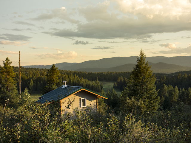 Small meditation retreat cabin with a green roof in a forested mountain valley at sunset, suited to a mighty meditator's month yoga retreat.