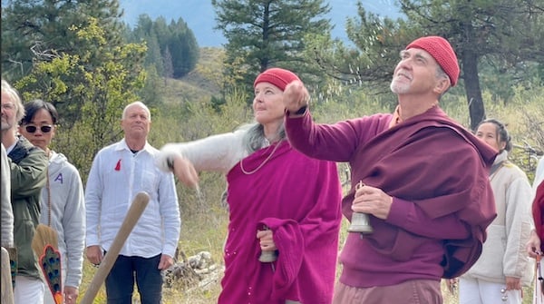 Outdoor Dharma community at a retreat, with two people in red hats gesturing beneath pine trees, reflecting Integral Evolution and 21st-Century Awakening.