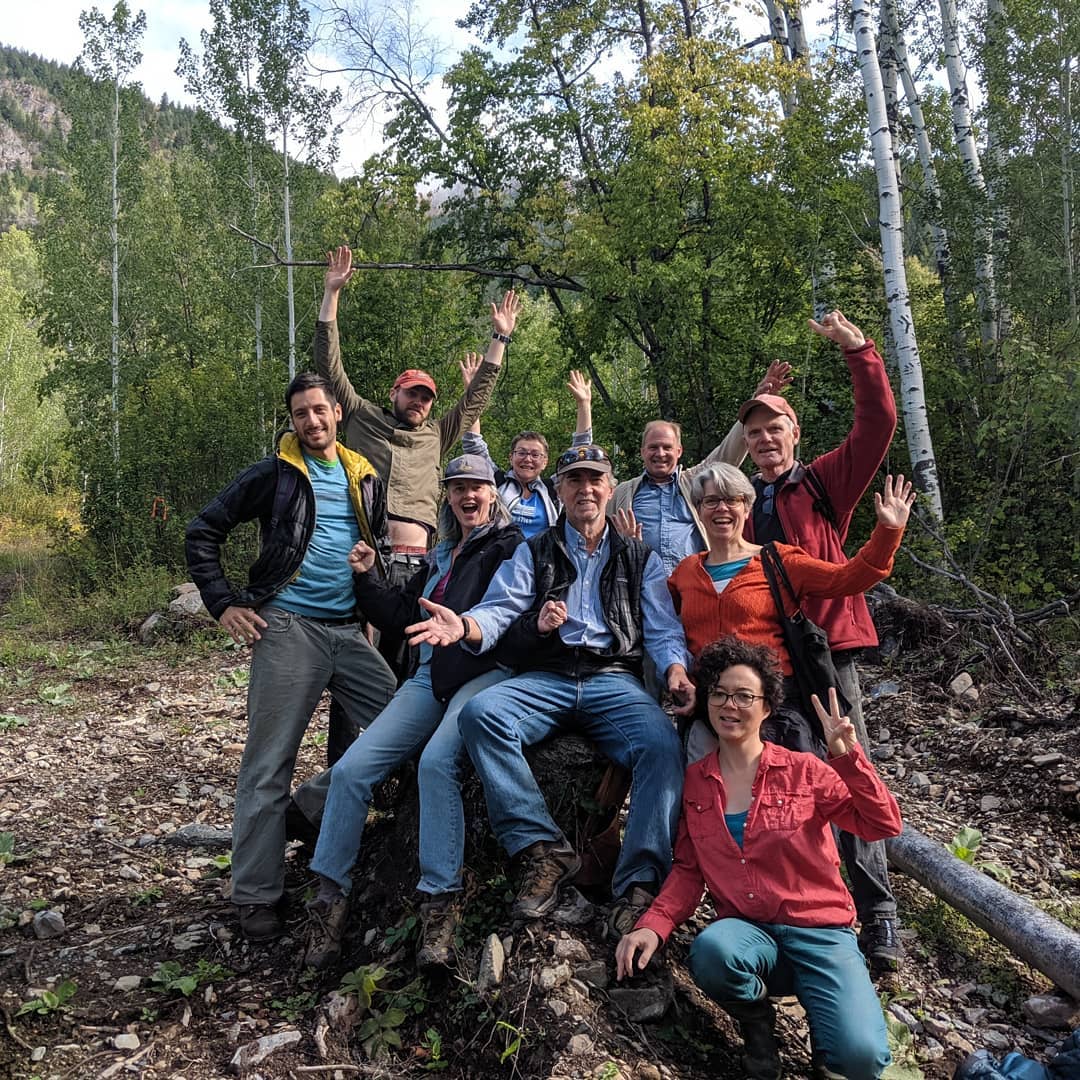 Smiling Dharma community gathered on a forest trail, raising hands in celebration of Integral Evolution and 21st-Century Awakening retreat practice