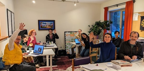 Dharma community gathered in a retreat room, waving during an Integral Evolution session on 21st-century awakening and sangha practice.