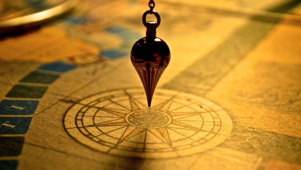 A metal pendulum hangs above a golden astrological chart, evoking Astro-Dharma, Saturn, discipline, and the path of spiritual mastery.
