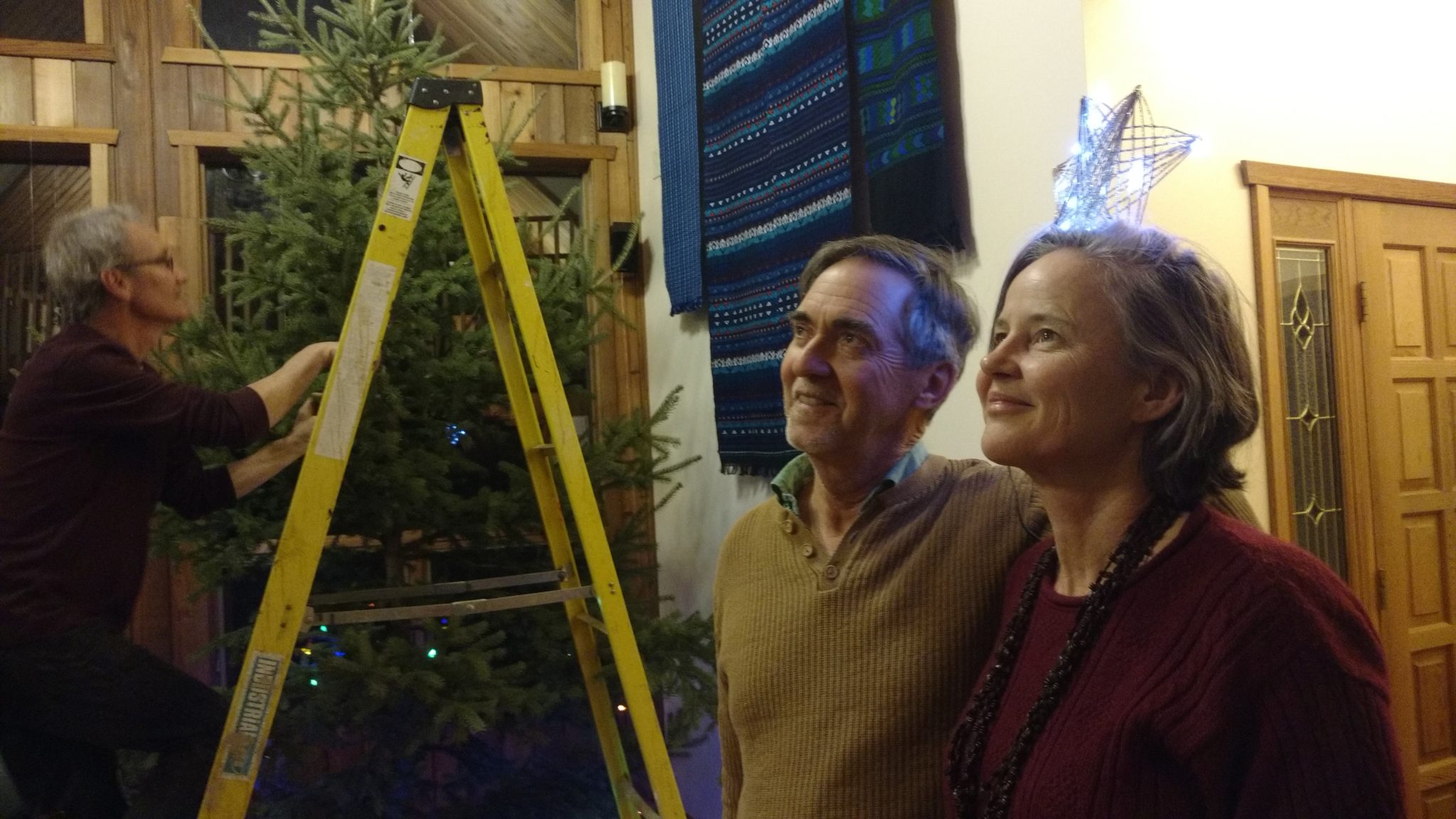 Dharma community members decorating a Christmas tree indoors, evoking Astro-Dharma themes of Saturn, discipline, mastery, and spiritual awakening.