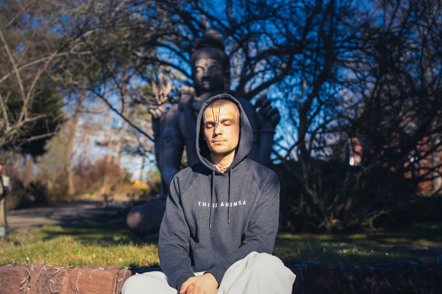 Man meditating outdoors with eyes closed before a Shiva statue, reflecting yoga, mantra meditation, mindfulness, and inner peace.