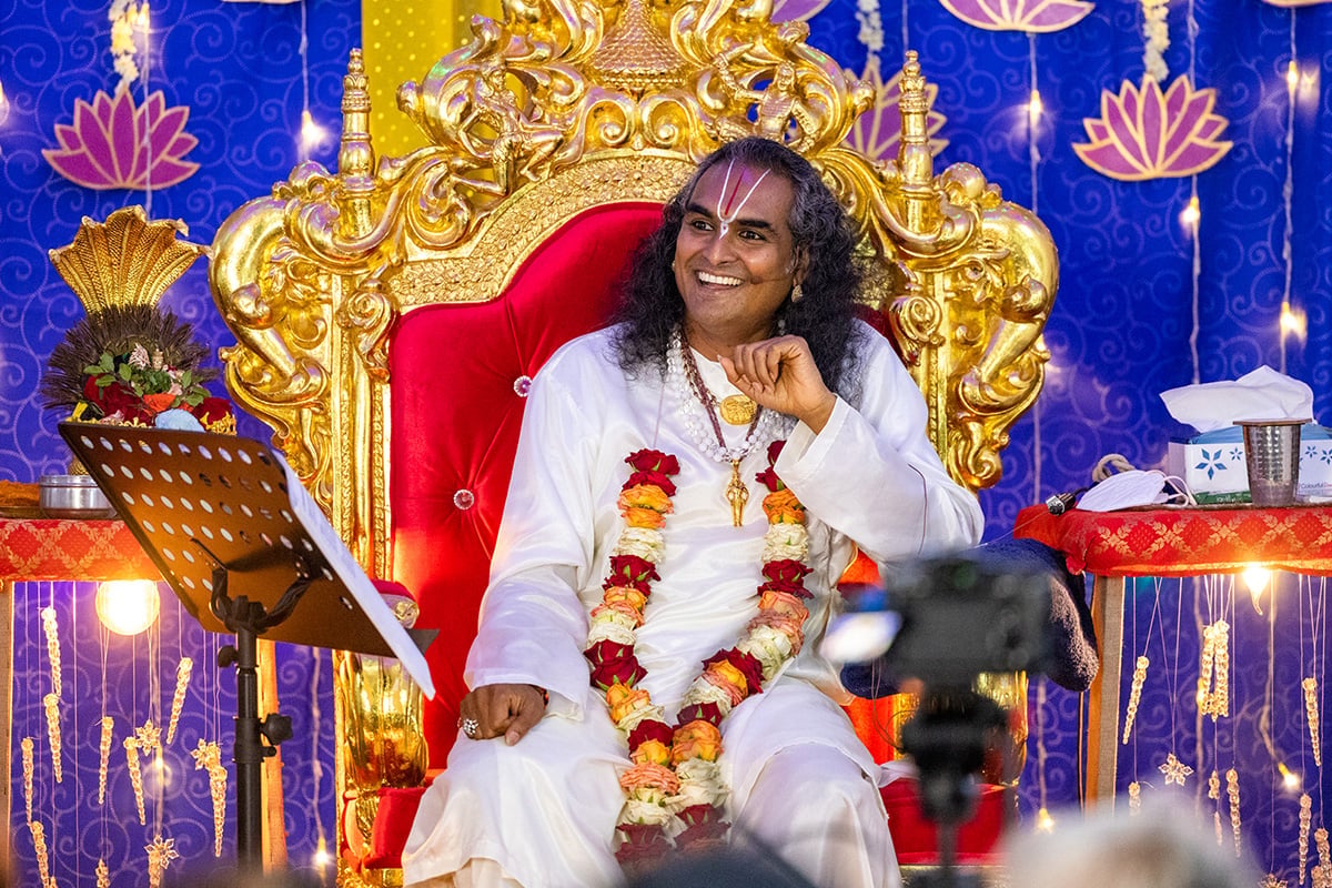 Paramahamsa Vishwananda seated on an ornate gold and red chair during a spiritual gathering, surrounded by flowers, lights, and devotional decor.