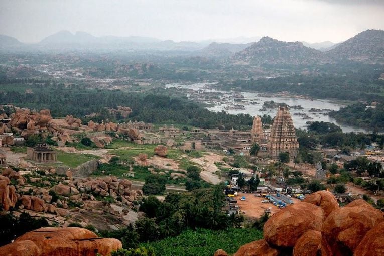 Panoramic view of Hampi's Vijayanagara ruins with temple towers, rocky hills, river landscape, and historic Bharatavarsha architecture.