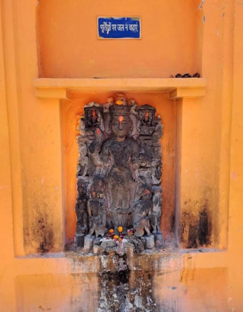 Weathered stone idol in an orange niche at Prithvinath Temple, Gonda, a Hindu temples heritage site, with offerings and a warning sign above.