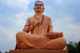 Terracotta statue of a seated Hindu saint, associated with Basavanna, holding a scripture against the sky during a Karnataka dharma pilgrimage.