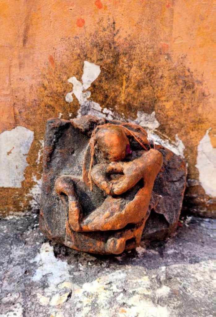 Weathered ancient idol fragment at Prithvinath Temple, Gonda, showing an eroded seated figure against a peeling wall for TEMPLE TRAIL hindu temples coverage