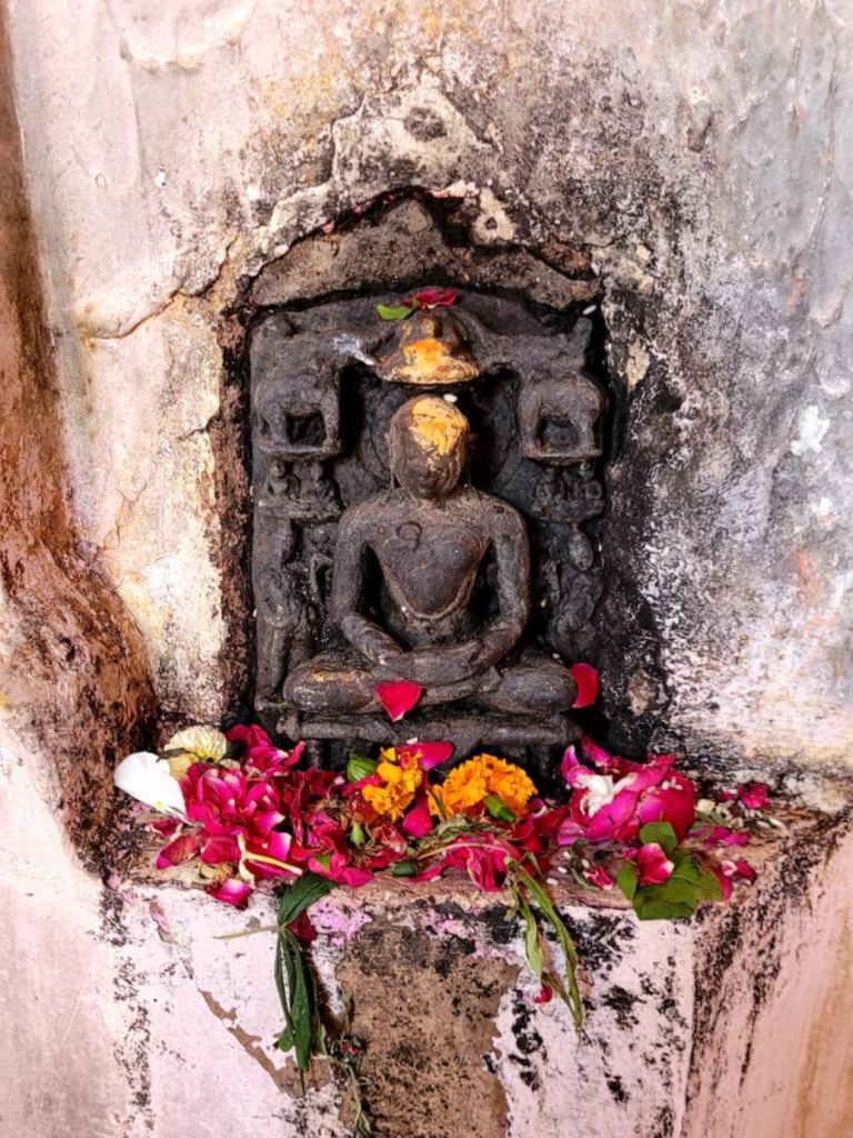 Weathered seated stone idol in a wall niche at Prithvinath Temple, Gonda, covered with chandan and flower offerings, part of TEMPLE TRAIL.