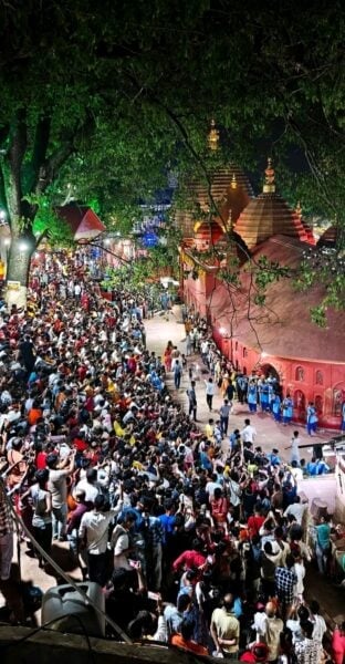 गुवाहाटी के कामाख्या मंदिर परिसर में रात के समय अंबुवाची मेले में उमड़ी श्रद्धालुओं की भीड़, रोशनी और लाल मंदिर संरचनाएं।