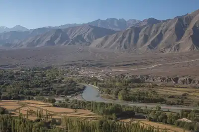 River valley with farms, trees, and arid mountain ranges, evoking the Indus basin and Bharat geopolitics around water sharing.