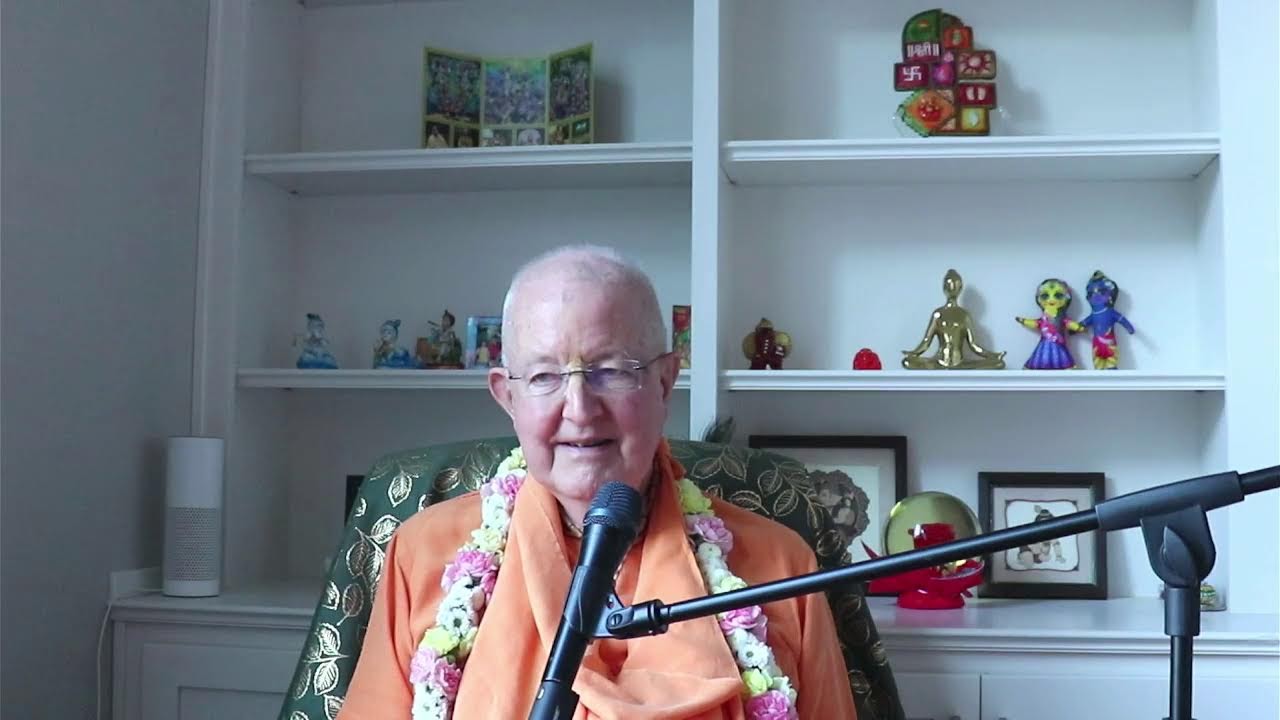 HH Romapada Swami speaks into a microphone during Respect Seminar Part 2, seated before shelves with devotional art and figures.