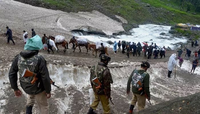 Security personnel watch pilgrims and pony caravans crossing a snowy Himalayan route during the Amarnath Yatra in Jammu and Kashmir, Bharat.