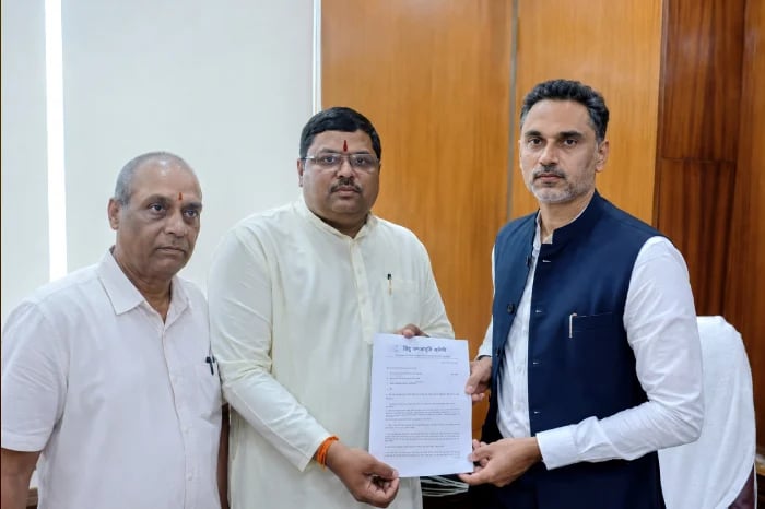 Three men indoors hold a written memorandum related to Bisur, Sangli, where Hindu families reportedly face continued harassment and seek police intervention.
