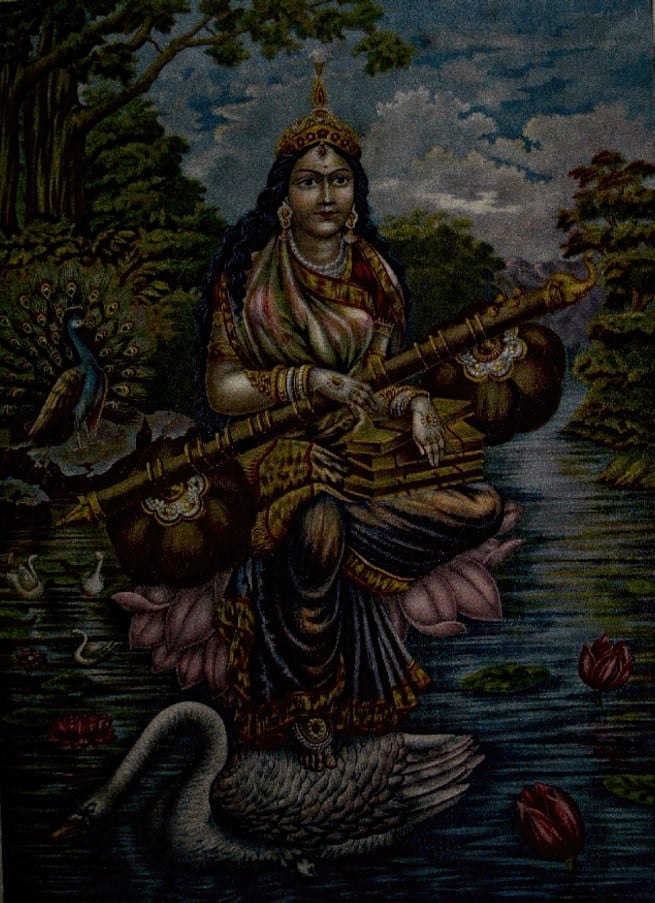 Traditional image of Goddess Saraswati seated on a lotus with a veena, swan, peacock, and river scene, symbolizing Sanskrit and Vedic knowledge.
