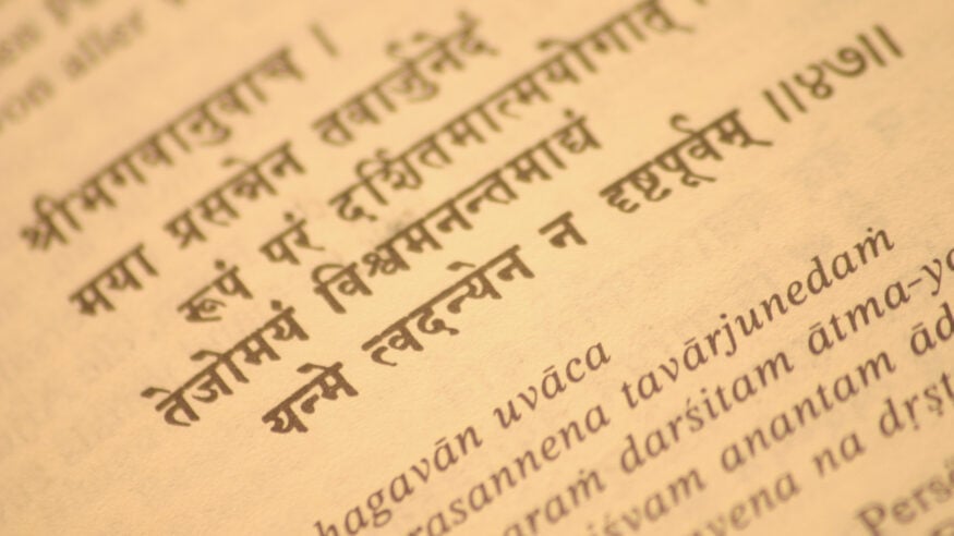 Close-up of Sanskrit Devanagari scripture with transliteration, evoking Hindu Dharma texts, Bharat, Bhagavad Gita and Yoga Sutra scholarship.