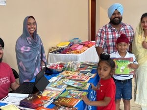 Sikh families and children gather beside a table of books and learning materials, reflecting Gurmat camp community life and S. Kuldeep Singh Ji’s legacy.