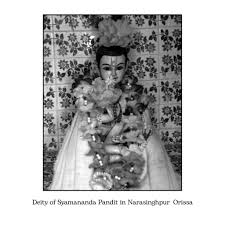 Black-and-white image of the Deity of Syamananda Pandit in Narasinghpur, Orissa, adorned with garlands and cloth before a patterned backdrop.