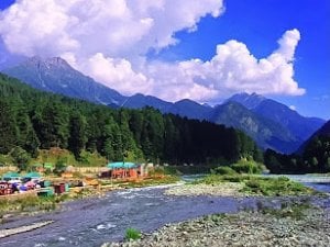 Mountain valley with a clear river, forested slopes, village buildings, and clouded Himalayan peaks, evoking Sikh heritage and Guru Hargobind Sahib’s legacy.