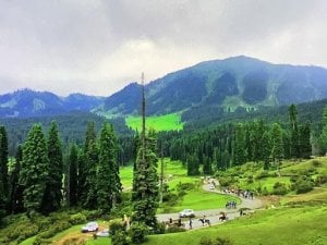 Lush green mountain valley with pine forests, cloudy hills, a winding path, and small groups of travelers, evoking Sikh heritage and Guru Hargobind Sahib.