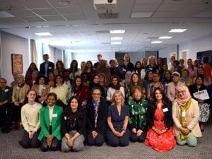 Large diverse group posing indoors after a community gathering, with attendees seated and standing, some in Sikh and South Asian dress.