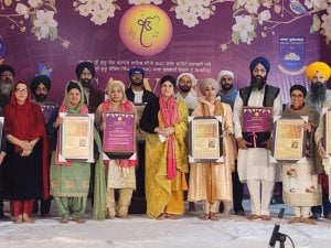Sikh community members on a decorated stage hold framed awards and Living Awake posters during a formal presentation ceremony.